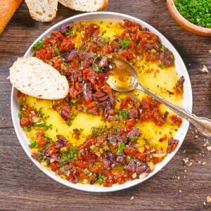 Mediterranean bread dip made with Kalamata olives, sun-dried tomatoes, and olive oil with a spoon on the plate and a toast point.