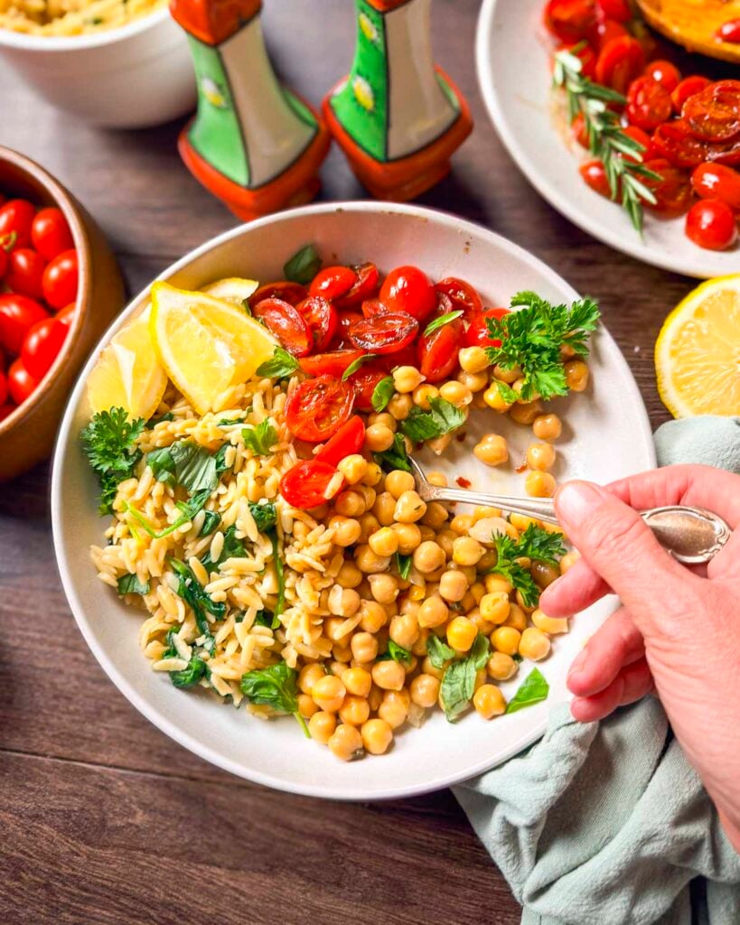 Chickpea orzo and blistered tomatoes in a bowl with a spoon in the bowl.