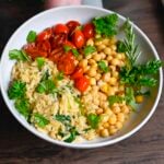 Chickpea orzo and blistered tomatoes in a bowl with a spoon in the bowl.