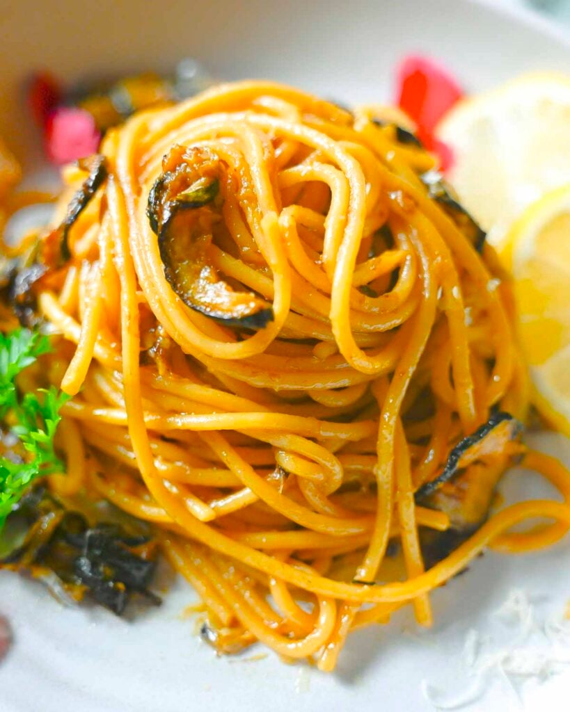 Spaghetti twirled with golden zucchini rounds on a while plate garnished with bread and lemon slices.