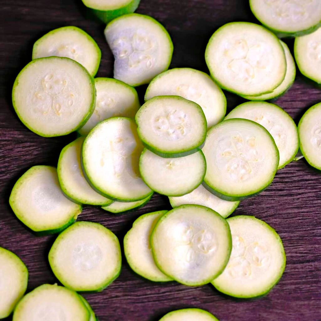 Thin zucchini slices in rounds on a wooden cutting board.