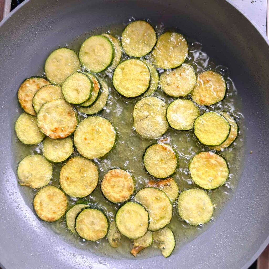 Zucchini slices in a skillet, frying in sunflower olive oil.