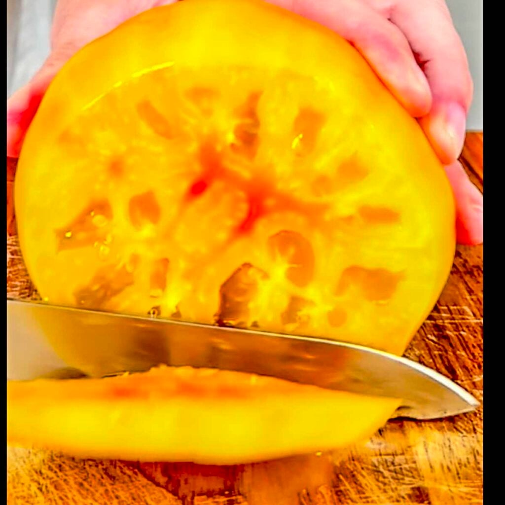 A knife cutting through a yellow heirloom tomato