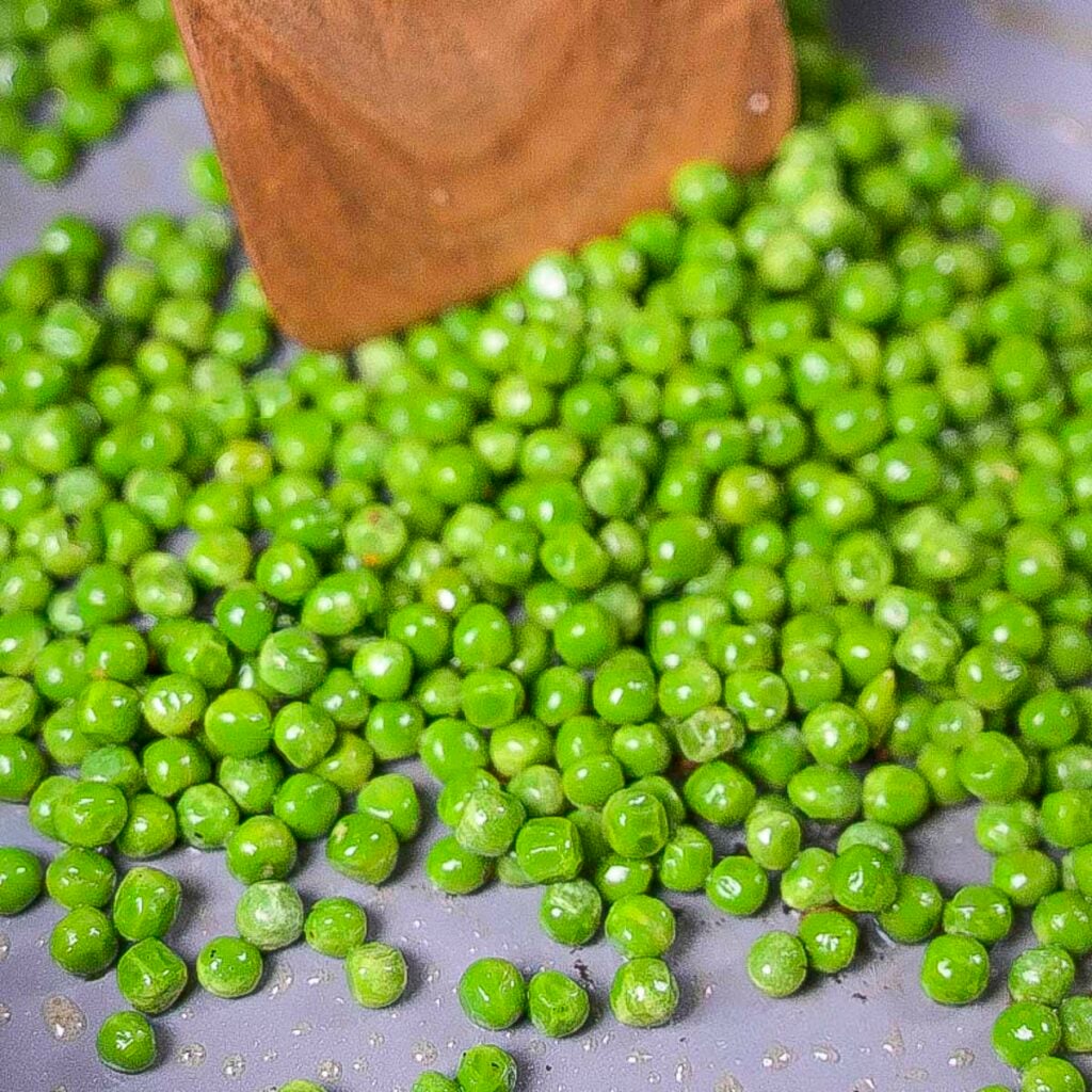 Mint peas in a skillet with a wooden spatula.