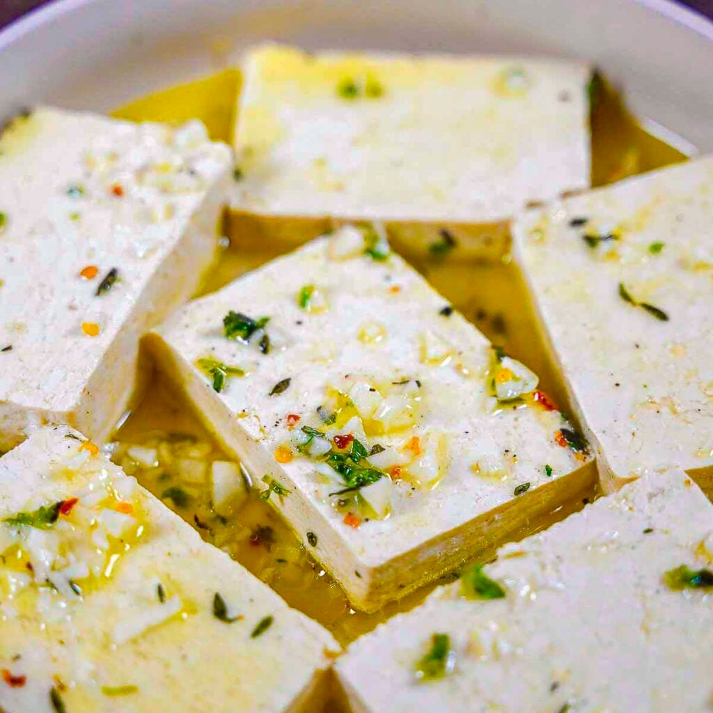 Six slabs of tofu marinating in olive oil, lemon, garlic, and oregano.