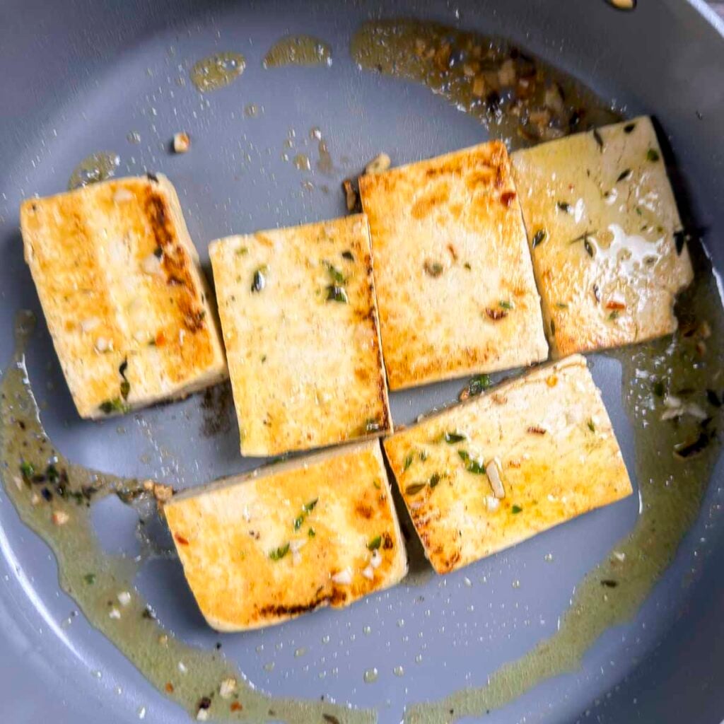 Six slabs of lemon tofu searing in a skillet.