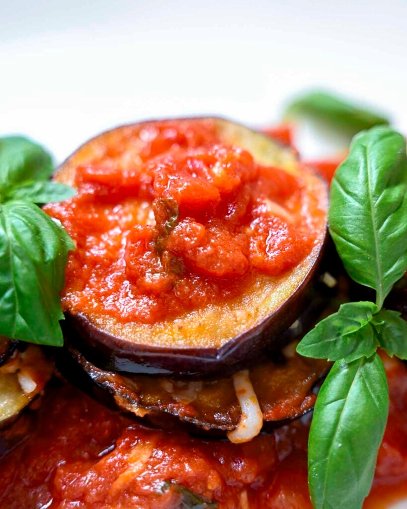 A single stack of eggplant Parmesan up close with San Marzano marinara sauce and fresh basil.