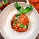 A stack of eggplant Parmigiana on a platter topped with torn basil leaves.