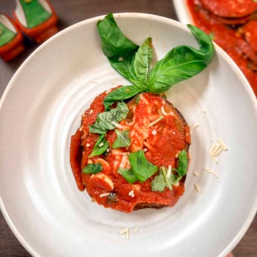 A stack of eggplant Parmigiana on a platter topped with torn basil leaves.