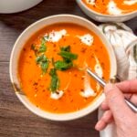 Vegan roasted red pepper tomato soup in a white bowl with torn basil leaves, red pepper flakes, and vegan heavy cream.