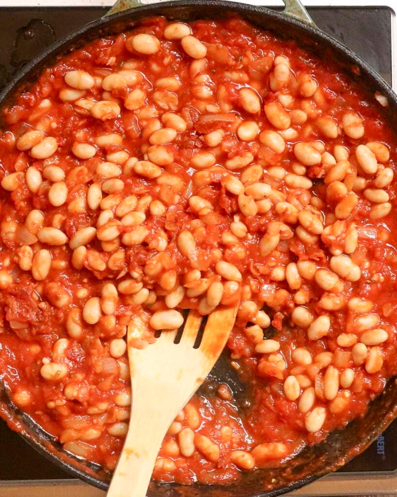 Saucy white beans in a skillet with a wooden spoon in the skillet.