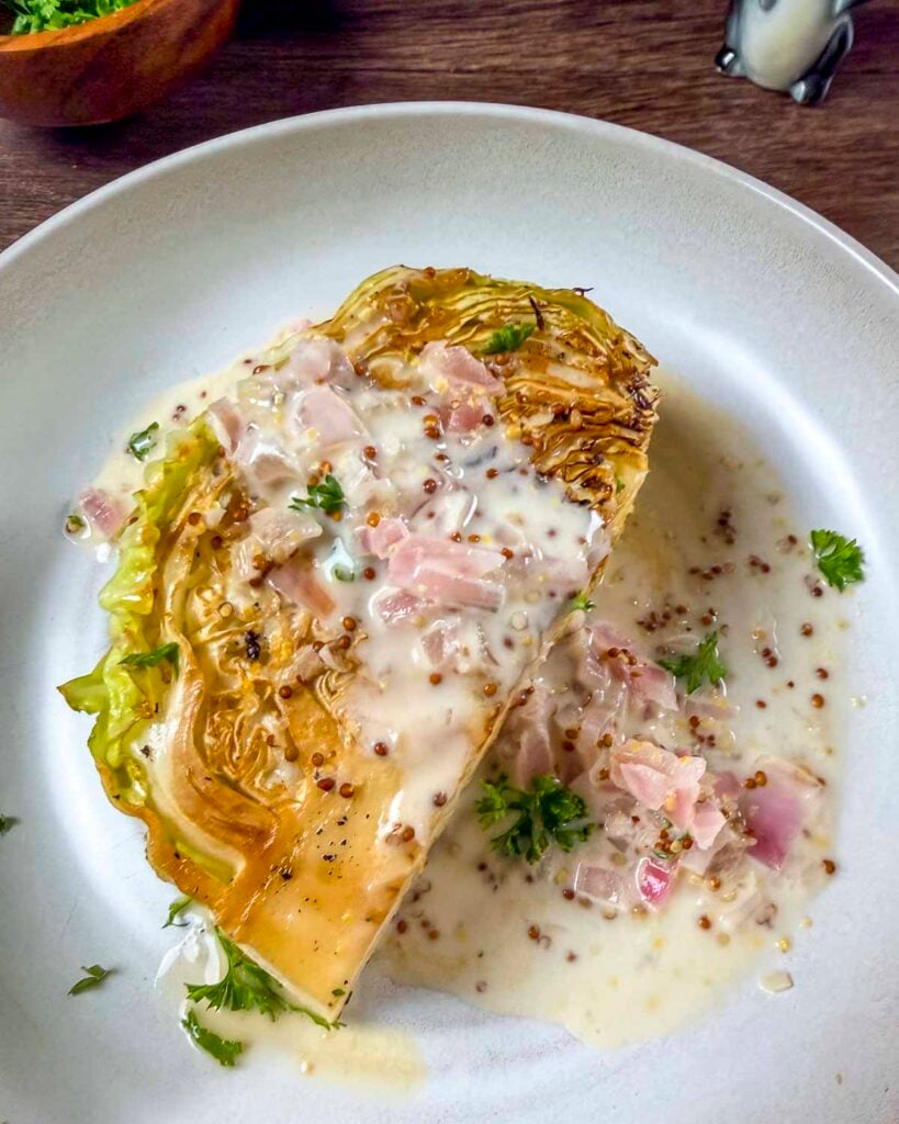 Charred cabbage wedge topped with a creamy white wine mustard sauce on a plate.