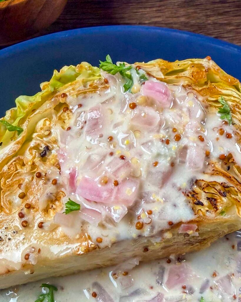 Charred cabbage wedge topped with a creamy white wine mustard sauce on a plate.