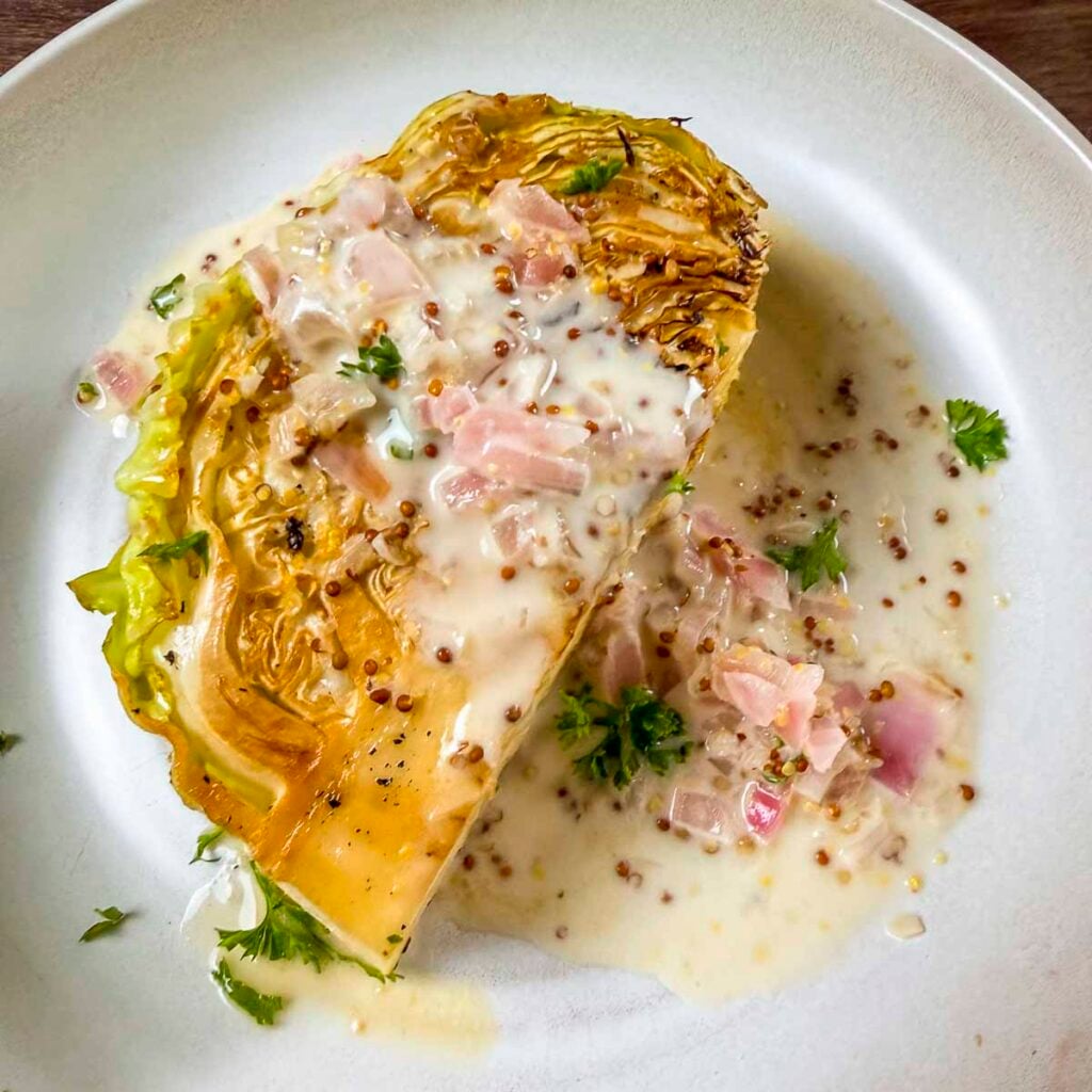 Braised cabbage wedge with white wine mustard sauce poured over the top of the wedge.