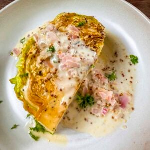 Braised cabbage wedge with white wine mustard sauce poured over the top of the wedge.