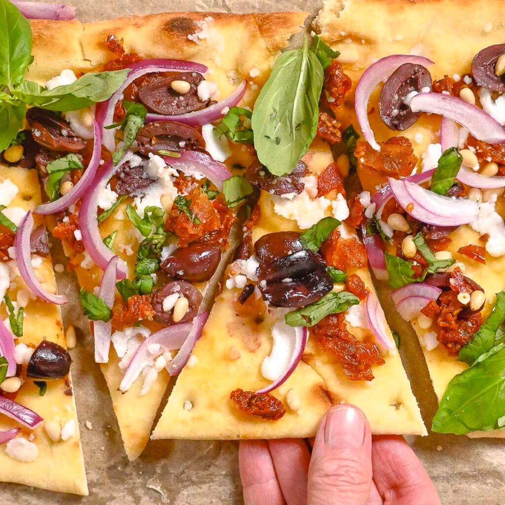 A hand reaching for vegan flatbread pizza on parchment paper.