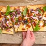 A hand reaching for vegan flatbread pizza on parchment paper.