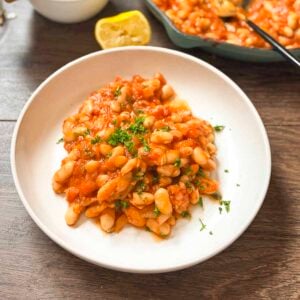 Mediterranean white beans on a plate with lemon and a skillet in the background.