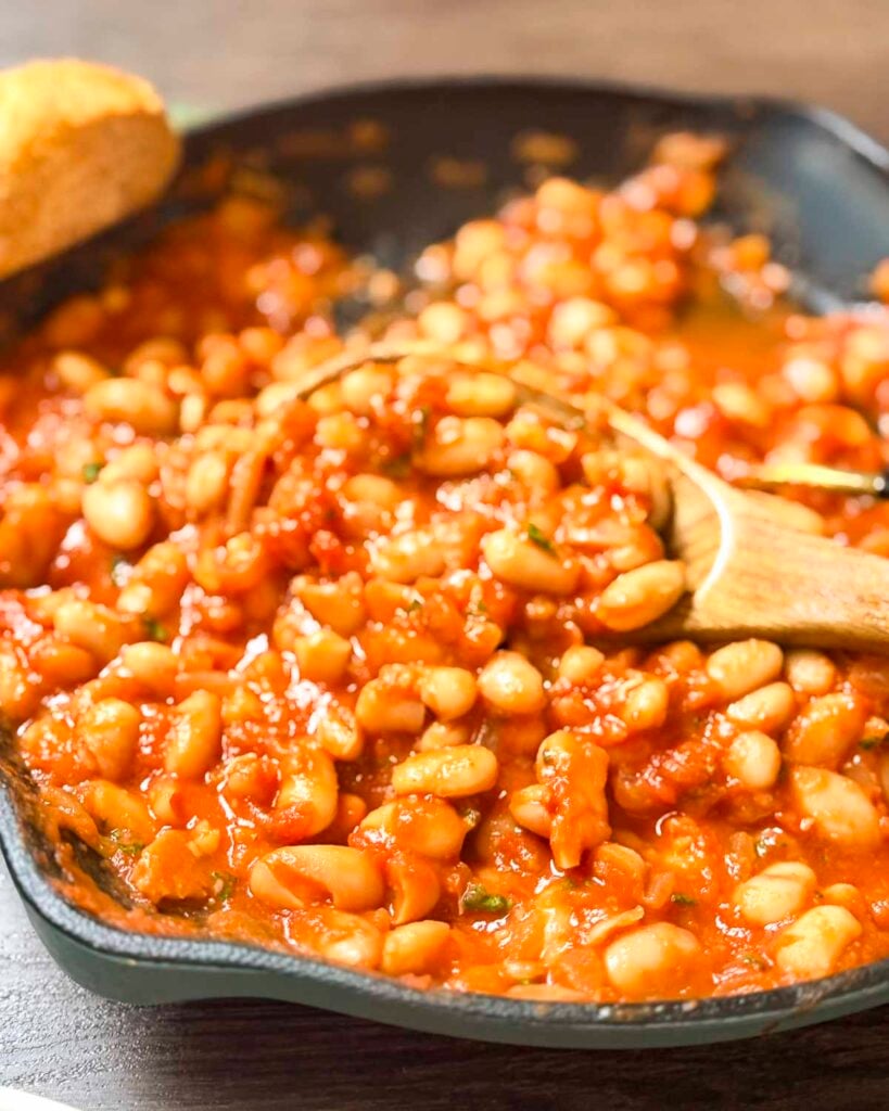 Mediterranean white beans In a skillet with a wooden spoon in the skillet.