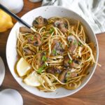 Mushroom pasta in a white bowl garnished with lemon and parsley.