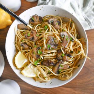 Mushroom pasta in a white bowl garnished with lemon and parsley.