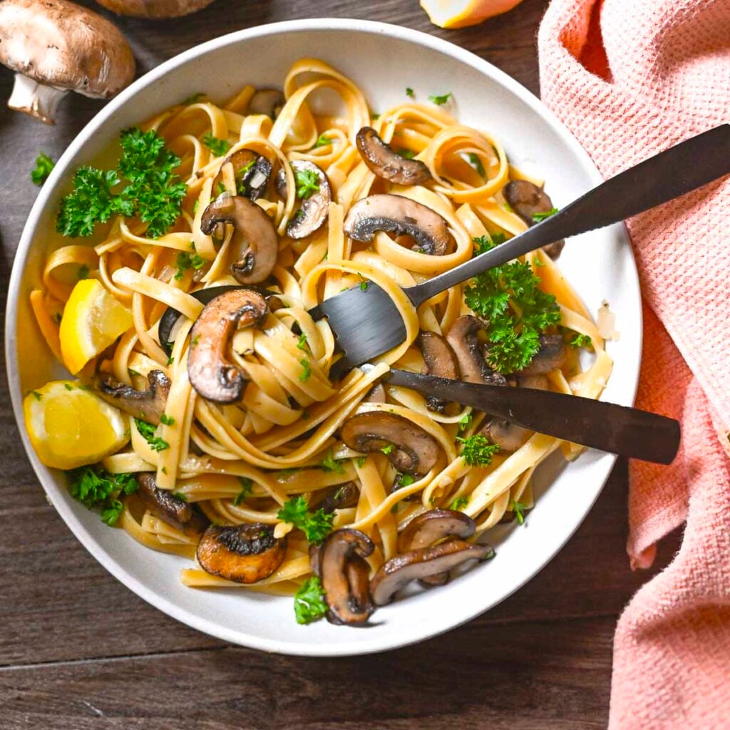 Mushroom pasta in a white bowl garnished with lemon and parsley.