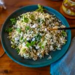 A green plate filled with spanakorizo, Greek spinach rice, that has been garnished with vegan feta cheese and fresh dill.