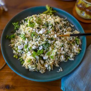 A green plate filled with spanakorizo, Greek spinach rice, that has been garnished with vegan feta cheese and fresh dill.